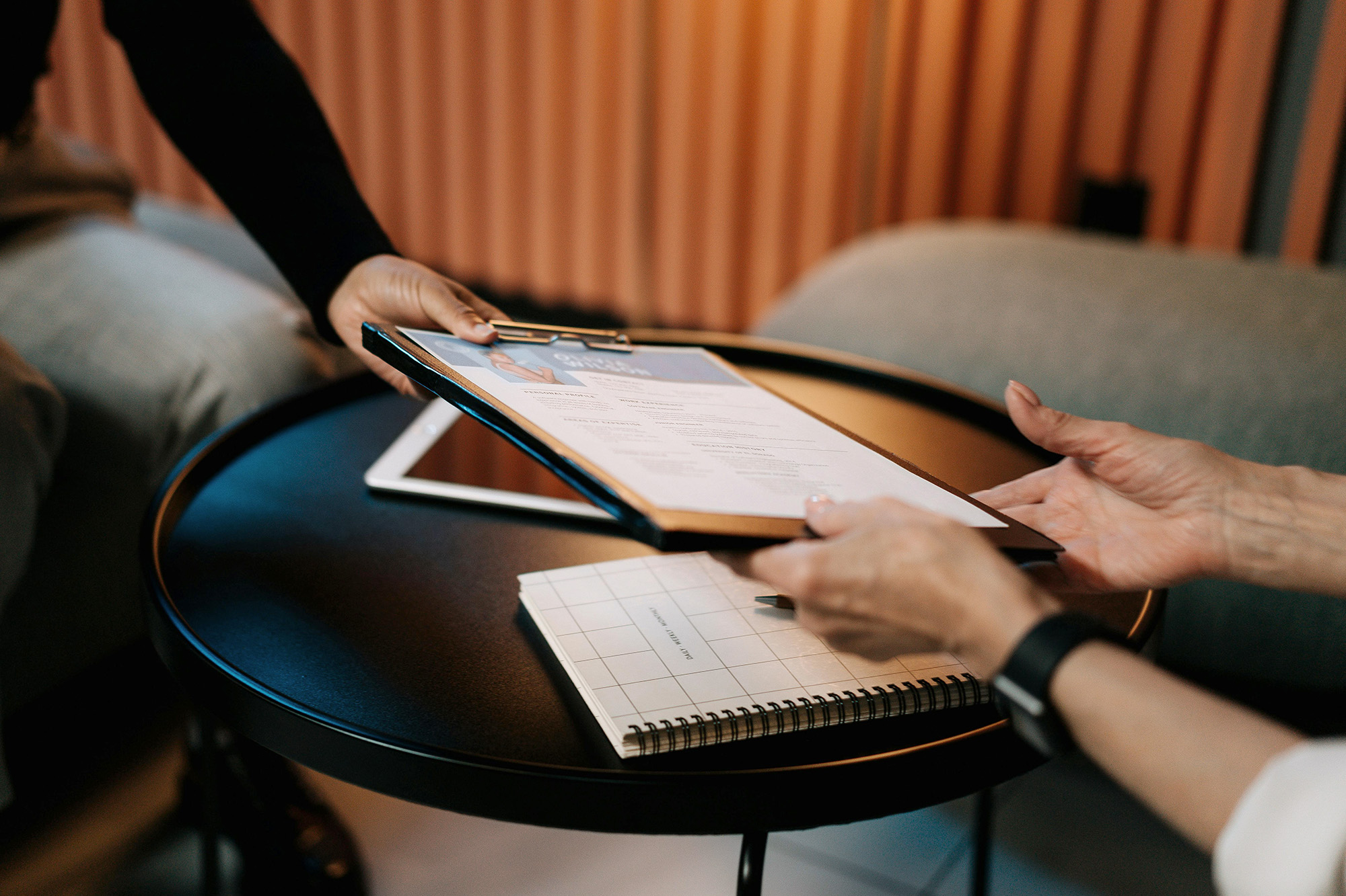 An applicant is providing a document similar to a resume to another person. Only the hands and arms are being shown.